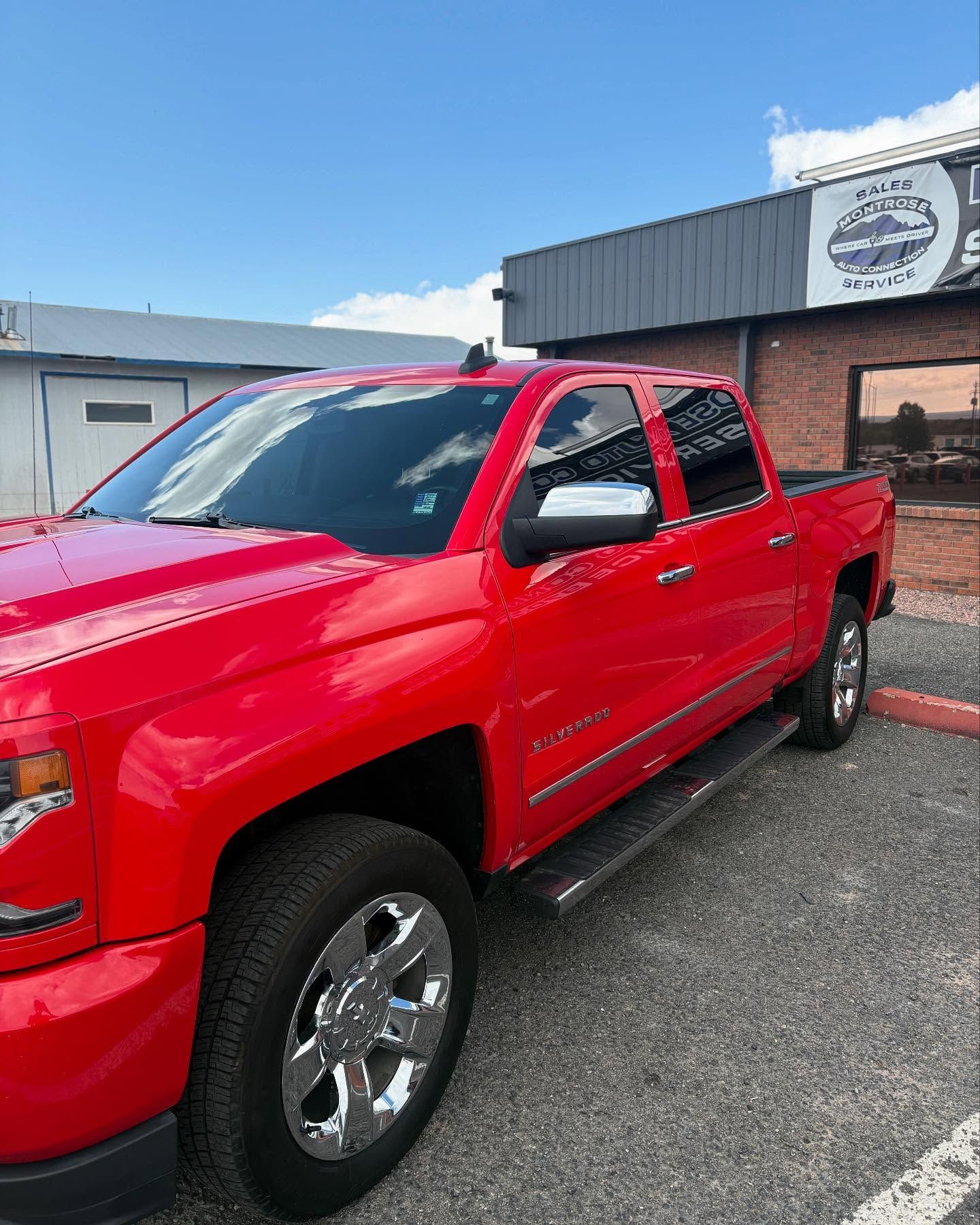 A bright red Chevrolet pickup truck parked outside a brick building on a sunny day.