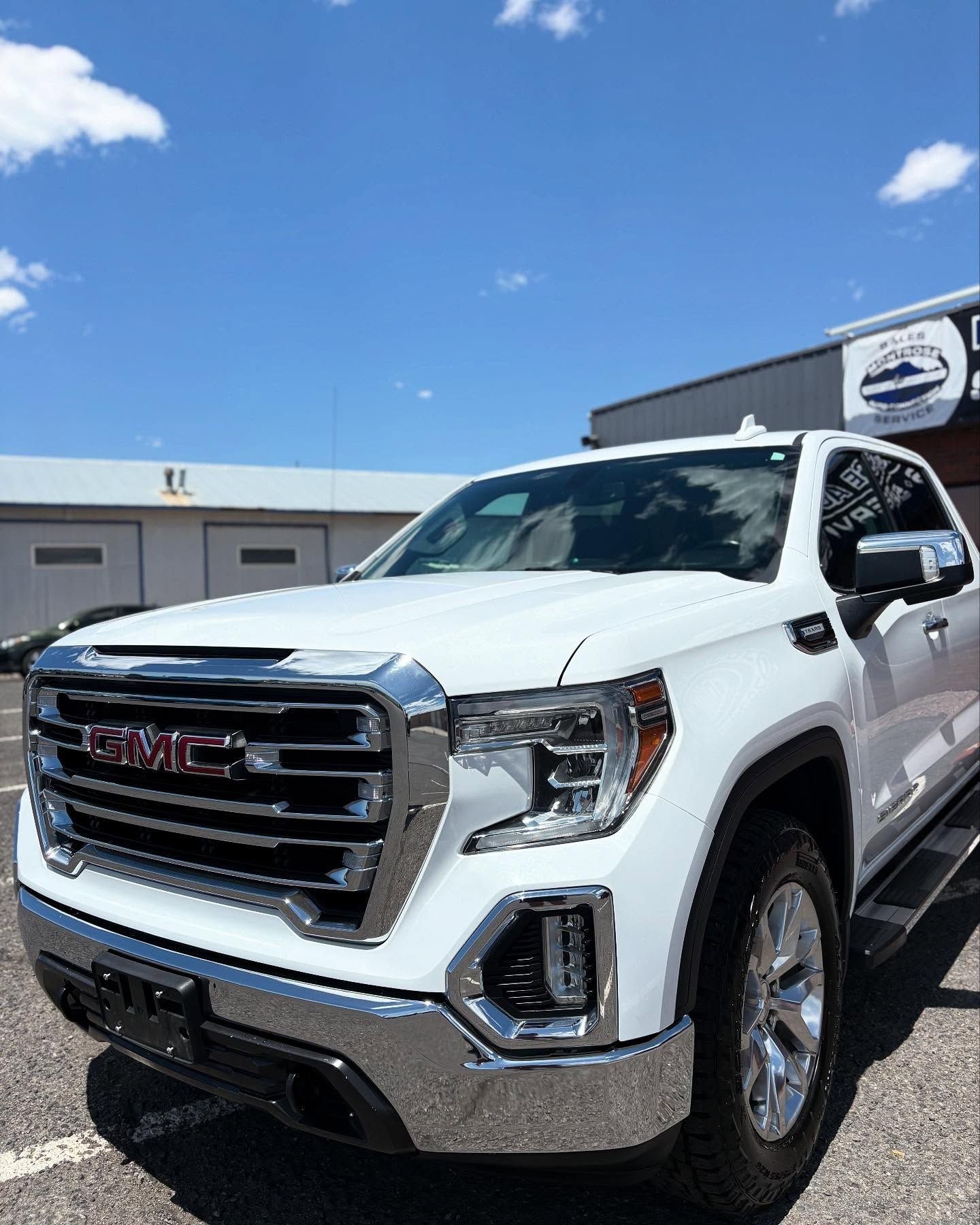A white GMC pickup truck parked in front of a business building under a clear blue sky.