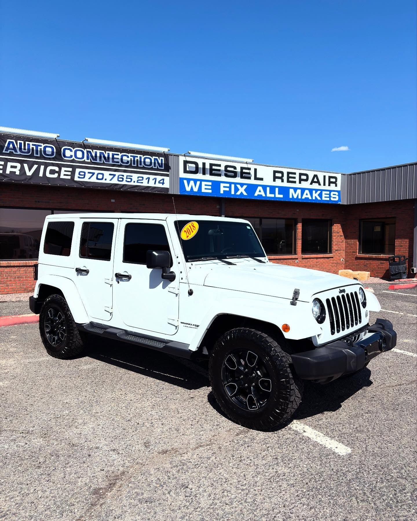 A white Jeep Wrangler parked in front of an auto repair shop with a blue sign that says 