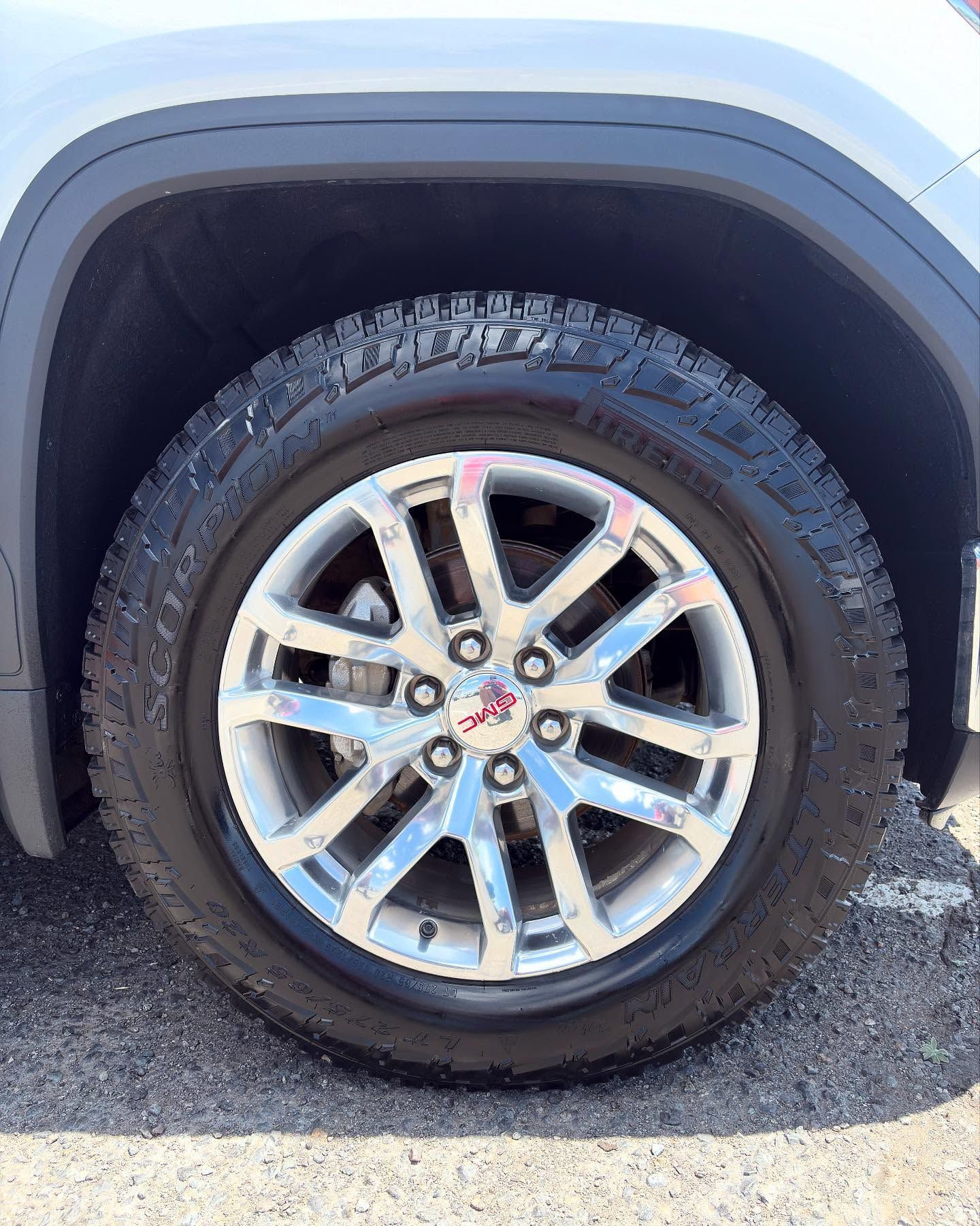 A close-up of a GMC vehicle tire with a chrome multi-spoke rim, set against a dark wheel well on a paved surface.