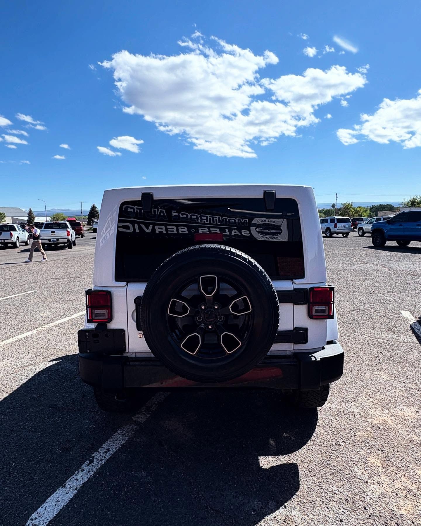 A white Jeep Wrangler parked in a gravel lot on a sunny day, viewed from directly behind.