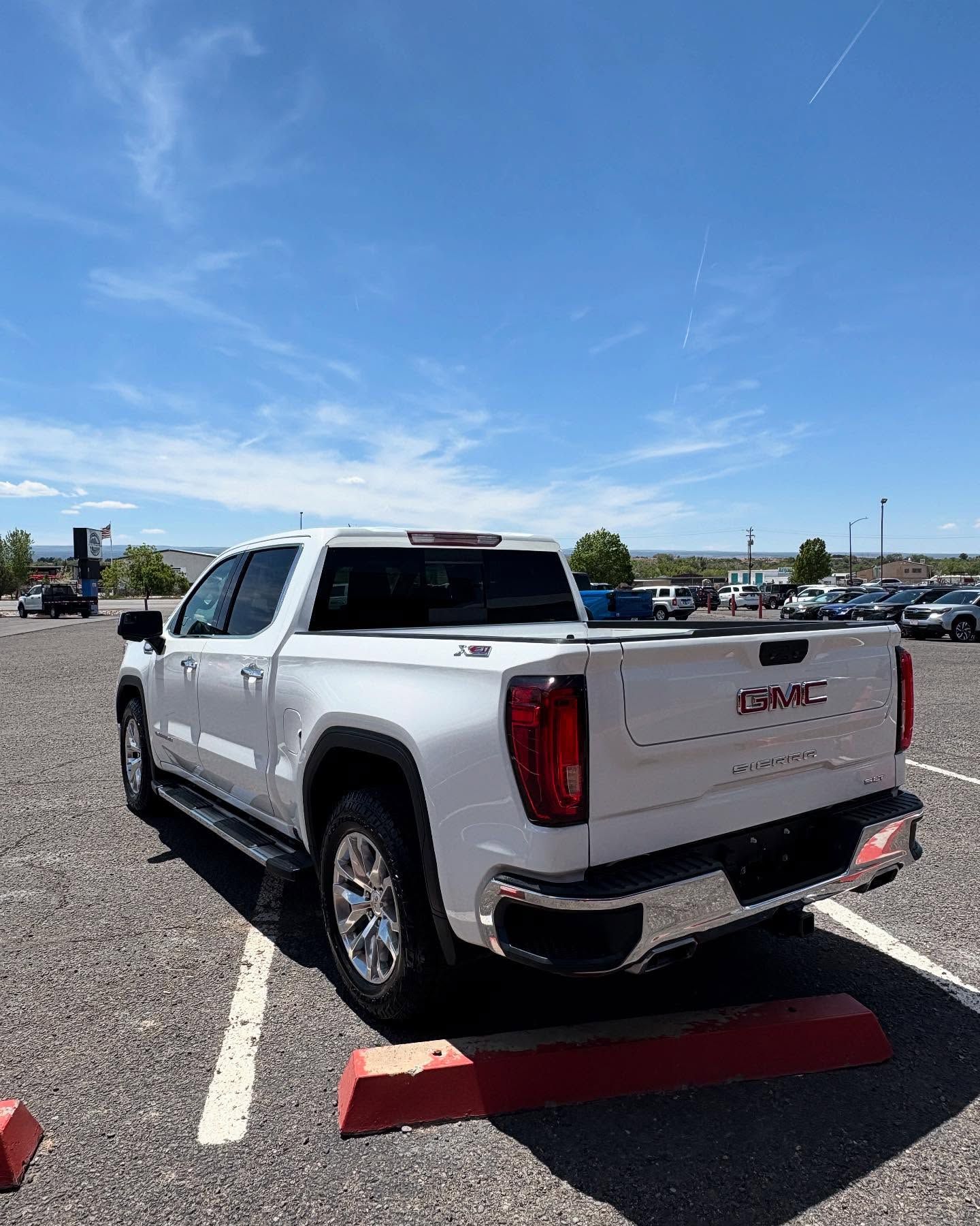A white GMC pickup truck parked in a gravel lot on a sunny day.
