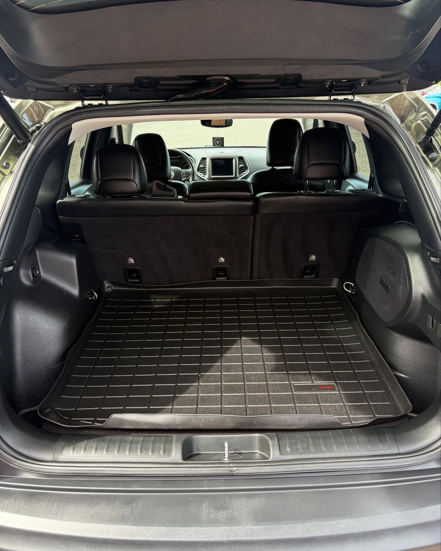 Interior view of an SUV trunk featuring black leather seats, a black all-weather cargo mat, and a speaker on the right.