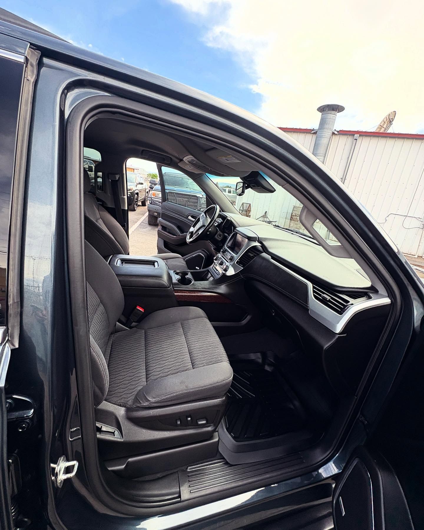 Interior view of a dark-colored vehicle through an open door, showing grey patterned front seats and the dashboard.