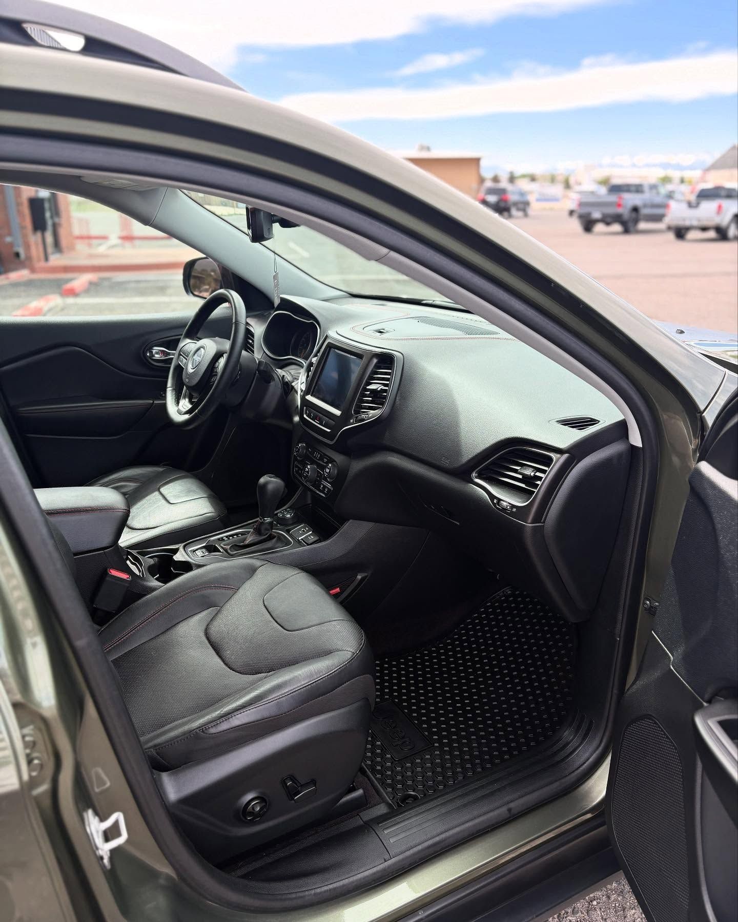 Driver-side view of a vehicle's dark gray leather interior, featuring a steering wheel, center console, and floor mats.