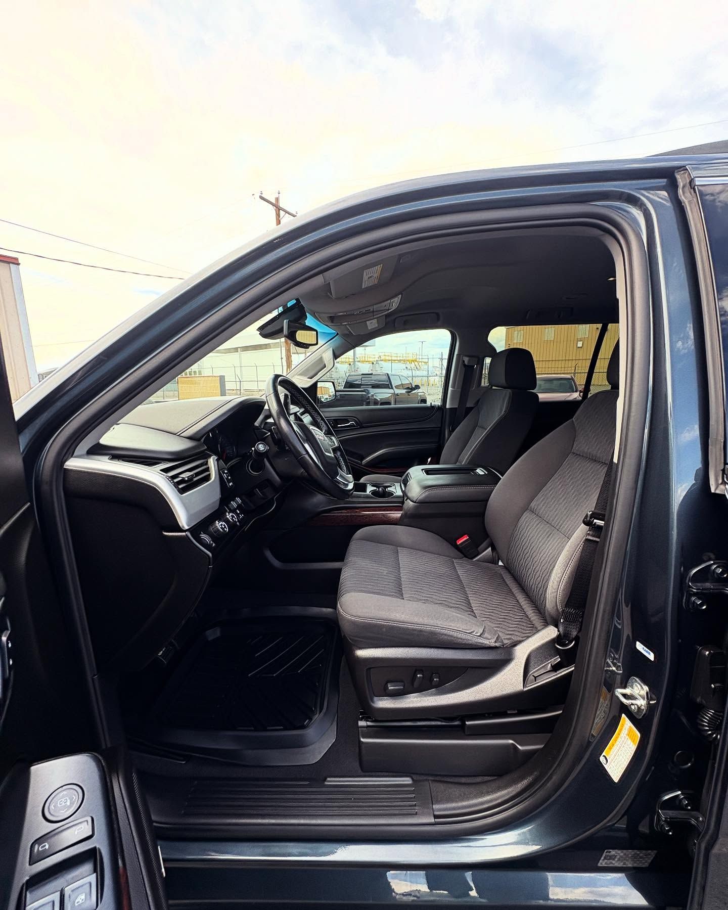 A view through an open car door into a dark gray interior with patterned cloth bucket seats and a modern dashboard.