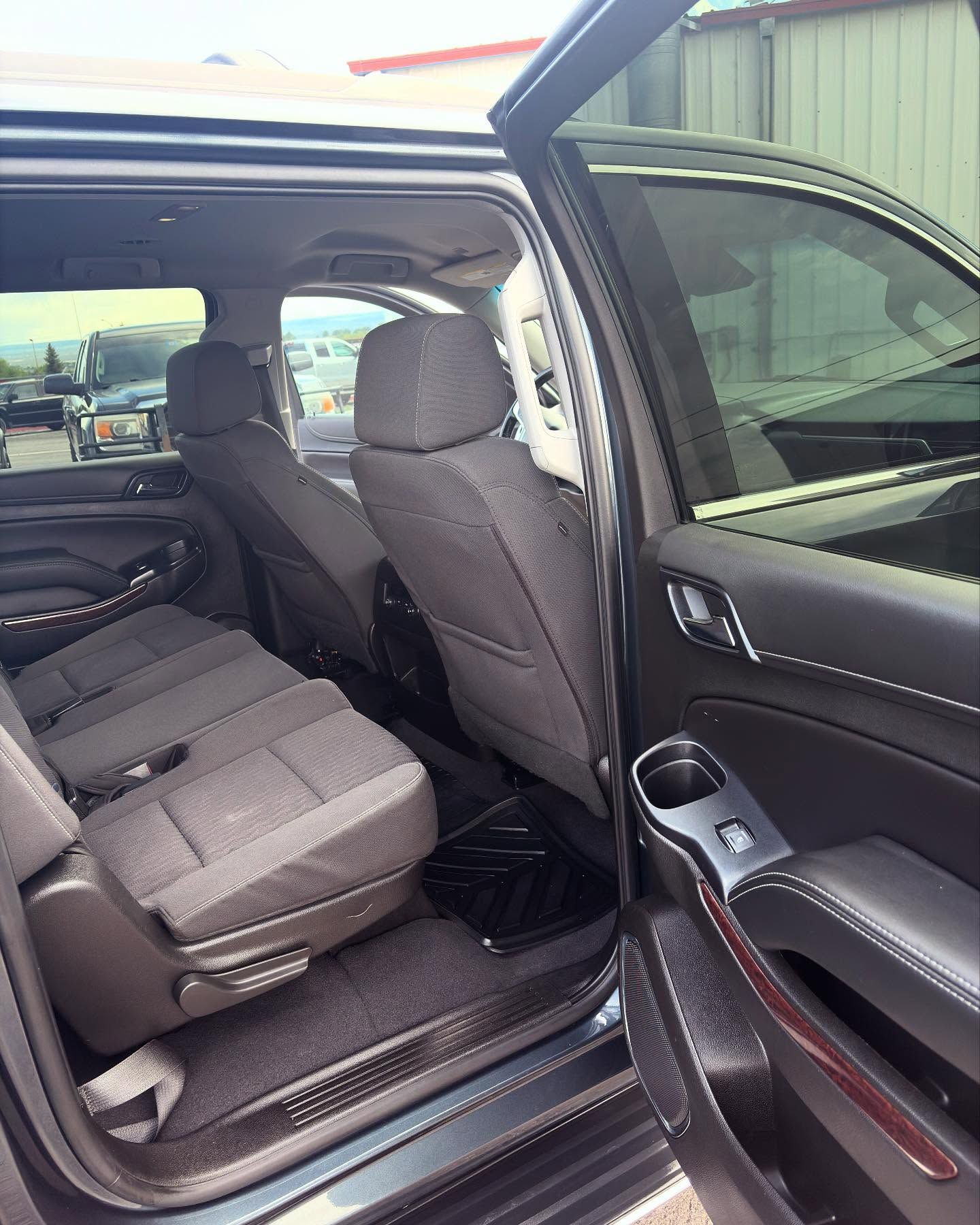 The open rear door of a dark-colored SUV shows a spacious cabin with gray fabric seats and black floor mats.