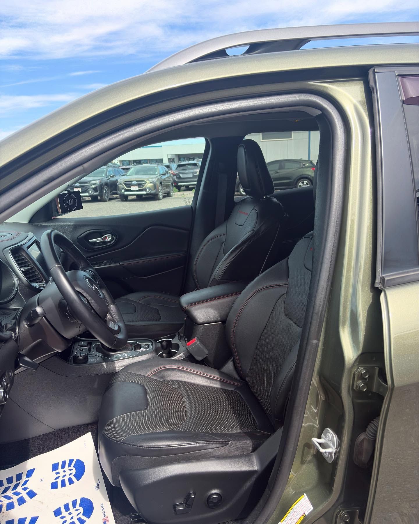 The interior of a green SUV with black leather seats, a steering wheel, and a parking lot visible through the window.
