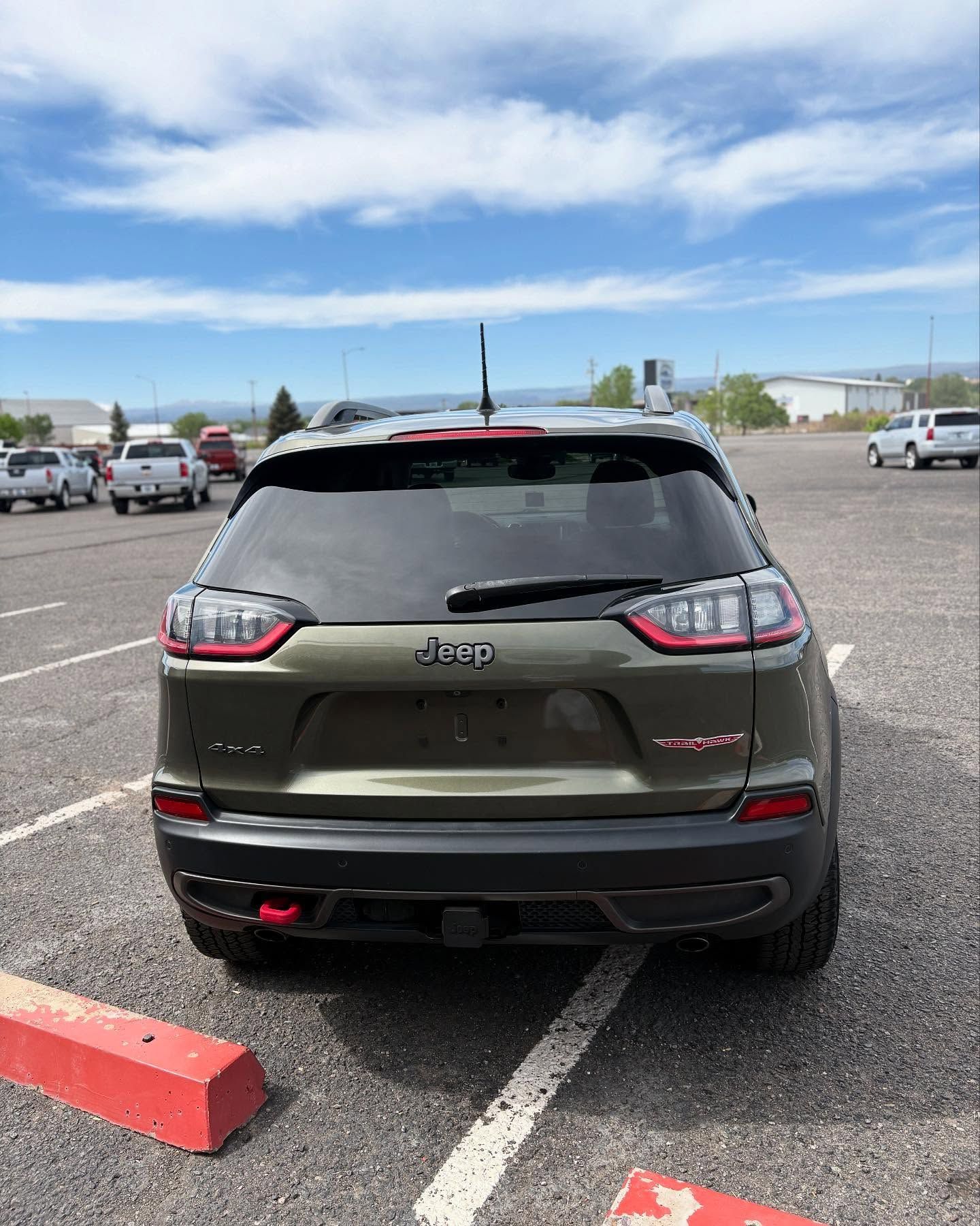 A green Jeep Cherokee Trailhawk parked in an outdoor lot on a sunny day.