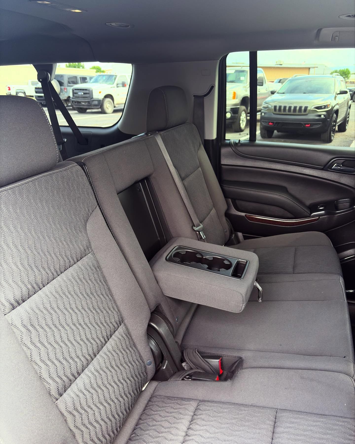 The interior view of a vehicle showing gray fabric back seats with a center armrest folded down, looking out at a car lot.