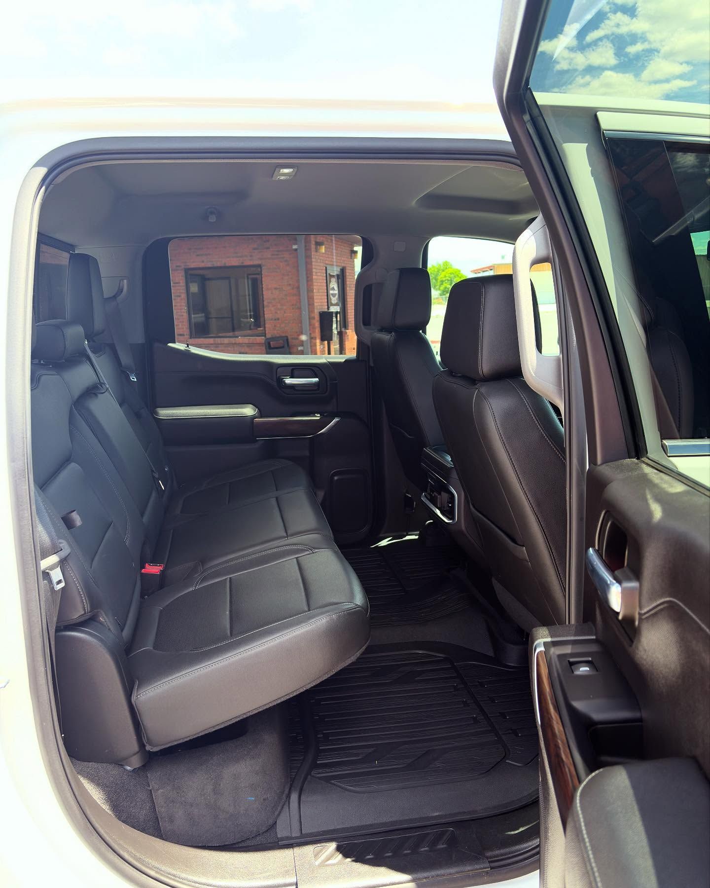 The back seat interior of a pickup truck with dark leather upholstery, all-weather floor mats, and an open side door.