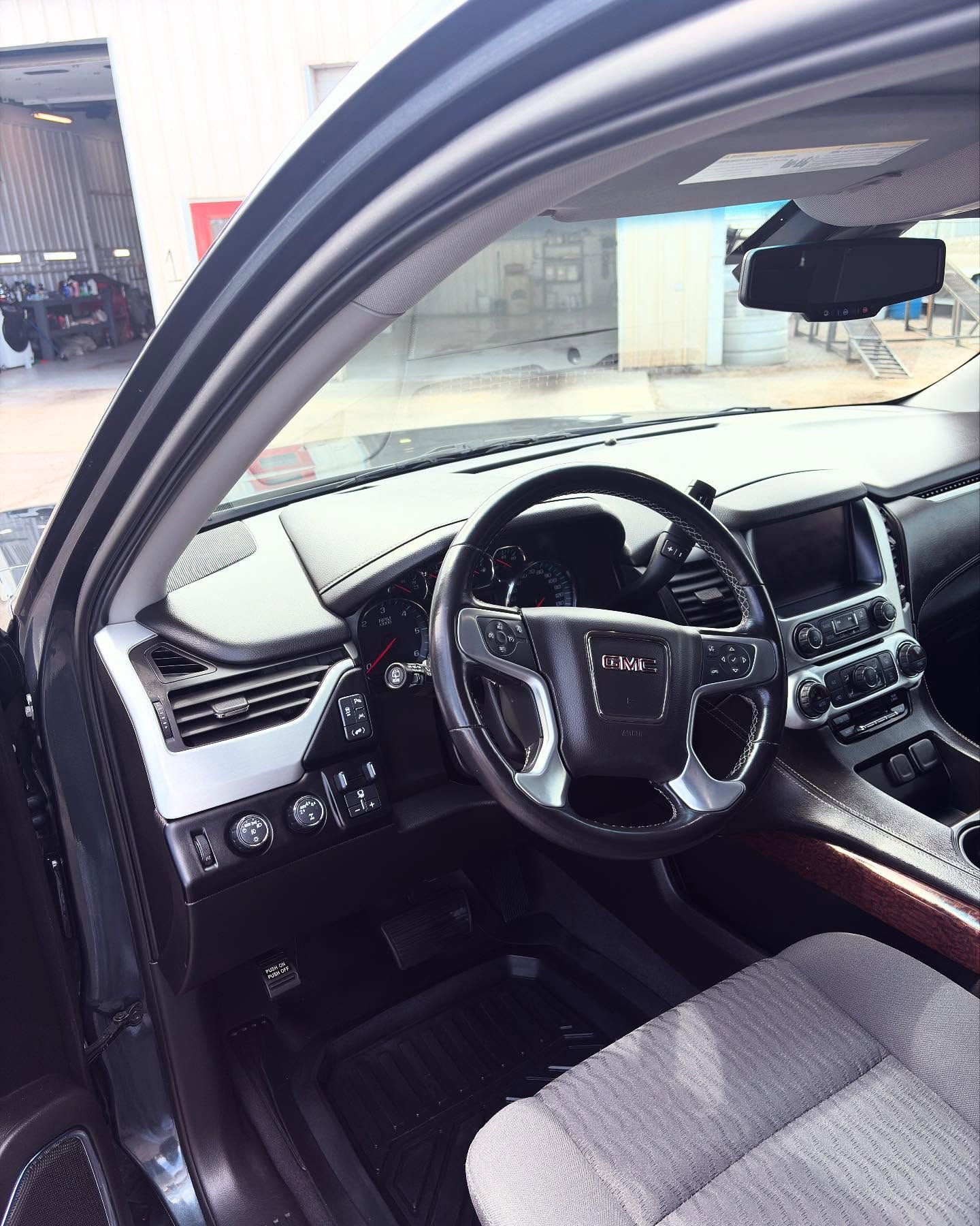 The interior of a dark-colored SUV, featuring a steering wheel, dashboard, infotainment screen, and cloth seats.