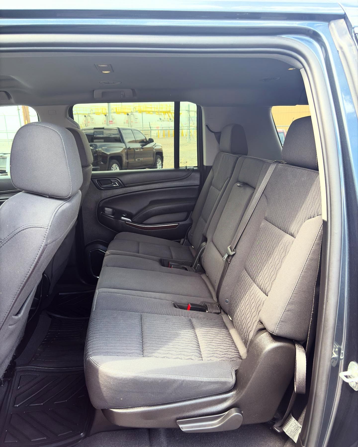 Interior view of a dark grey cloth backseat of a vehicle, showing two rows of seats.