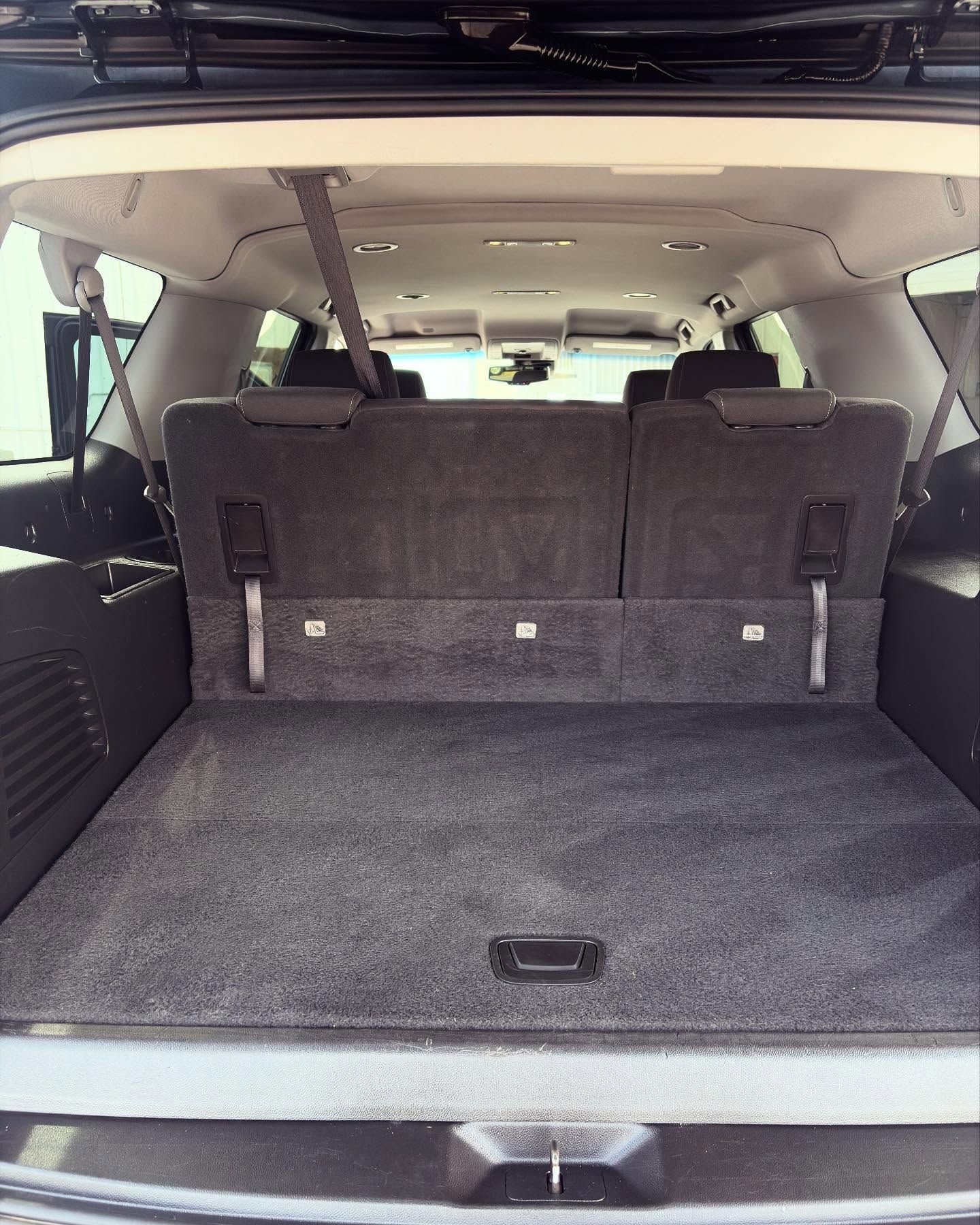 The open cargo area of a dark grey SUV, showing the back of the folded third-row seats and grey carpeted floor.