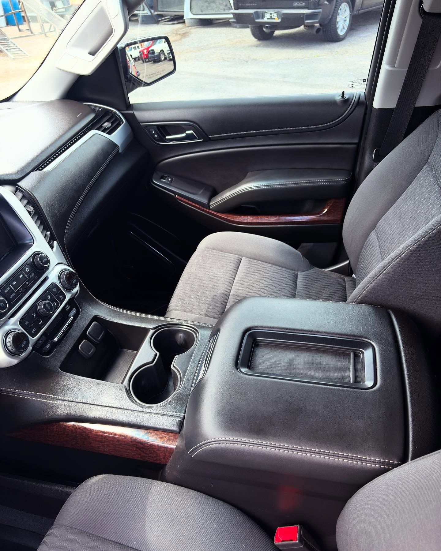 A front-passenger view of a modern vehicle interior, featuring gray cloth seats, a dark dashboard, and cup holders.