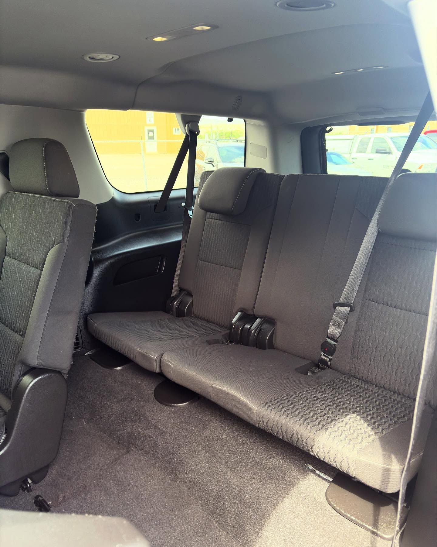 The interior back seats of a vehicle, showing a dark gray row of three seats and an adjacent seat in the foreground.