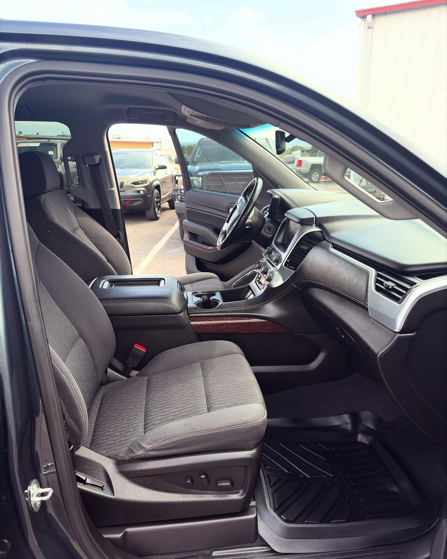 Interior view of a vehicle with dark gray fabric seats, black floor mats, and a dashboard with wood-grain trim.