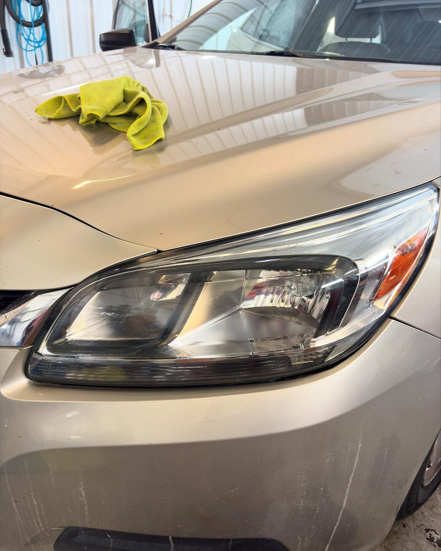 A beige car with a yellow microfiber cloth resting on its hood, next to a clean, clear headlight.