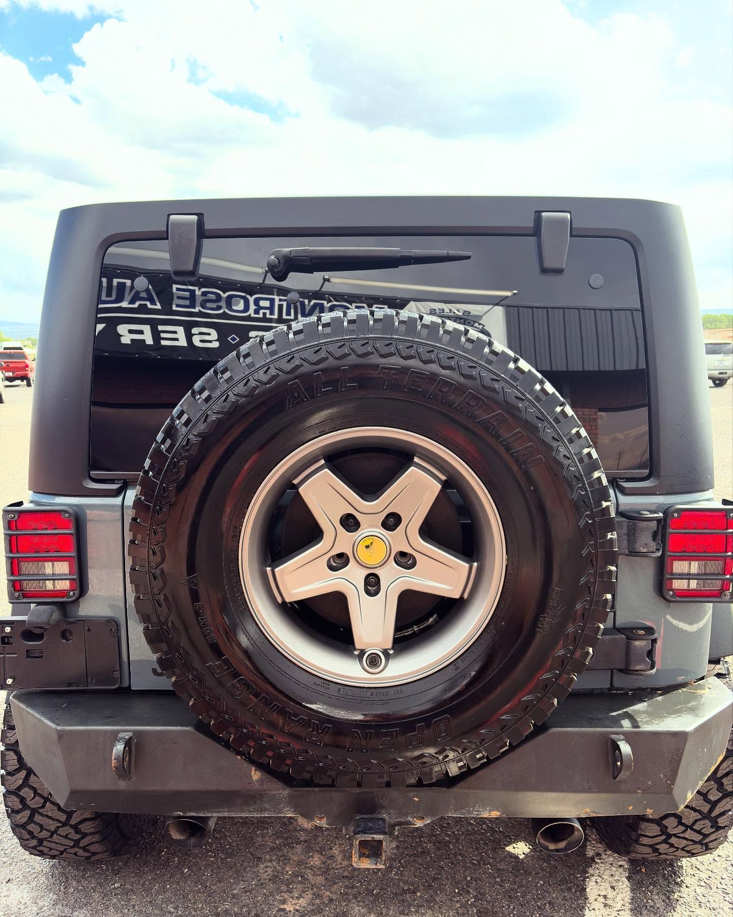 Rear view of a grey Jeep Wrangler with an aftermarket bumper and a spare tire mounted on the tailgate.