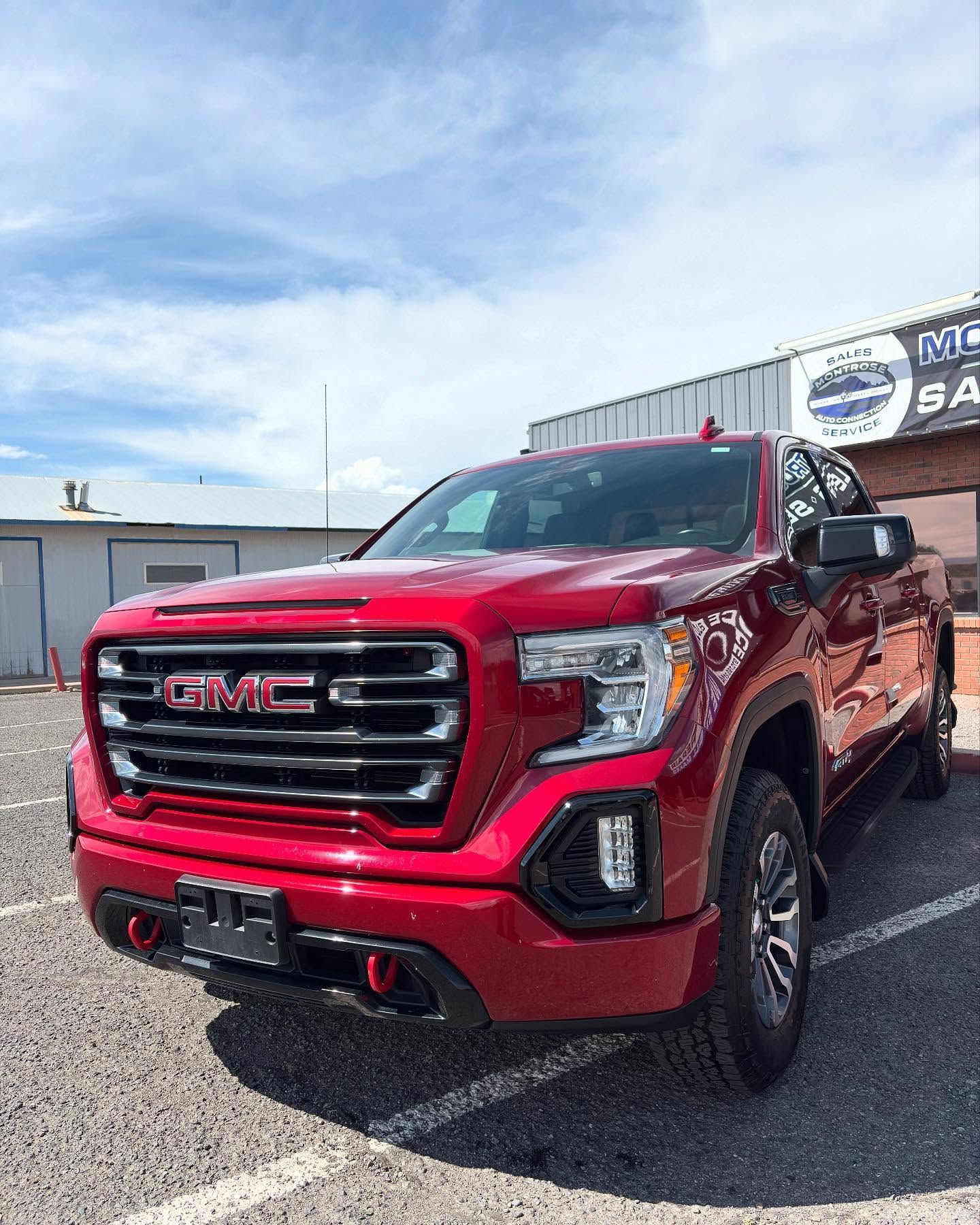 A red GMC Sierra pickup truck parked on a gravel lot under a blue sky on a sunny day.