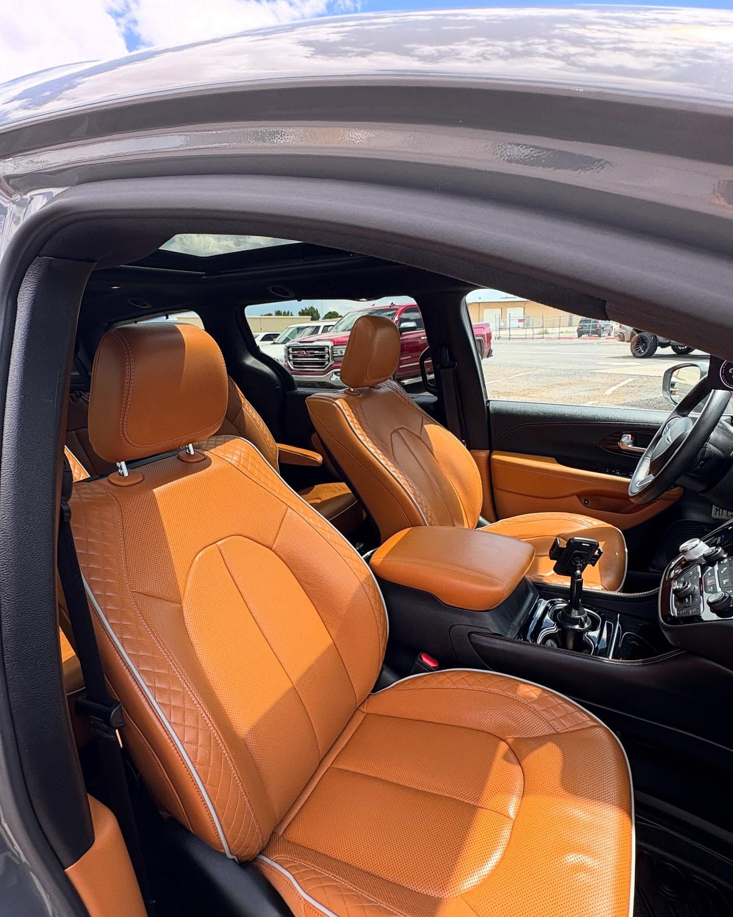 Tan leather seats with a textured pattern inside a car, featuring a panoramic sunroof and a view of a parking lot outside.