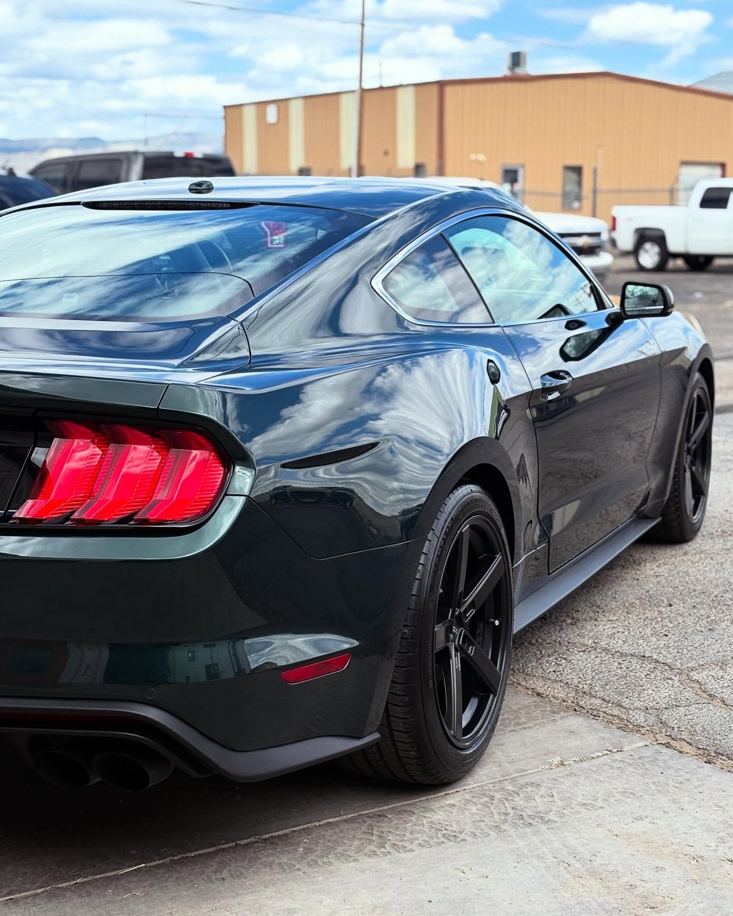 A dark green Ford Mustang parked outdoors, shown from a rear three-quarter angle with black wheels.