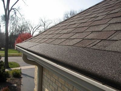 Close-up of a shingled roof edge with gutters above a brick house exterior.