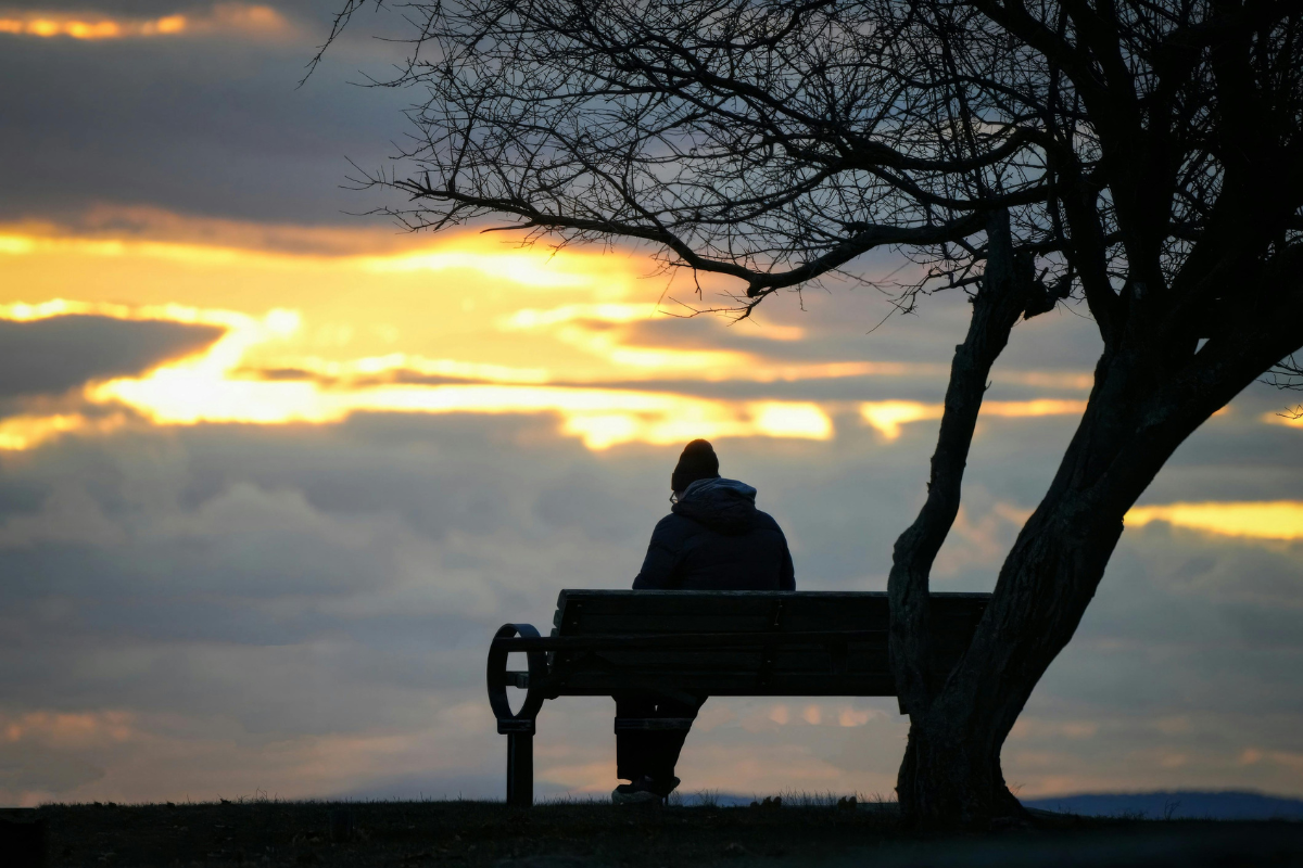 A man sits alone on a park bench at sunset.