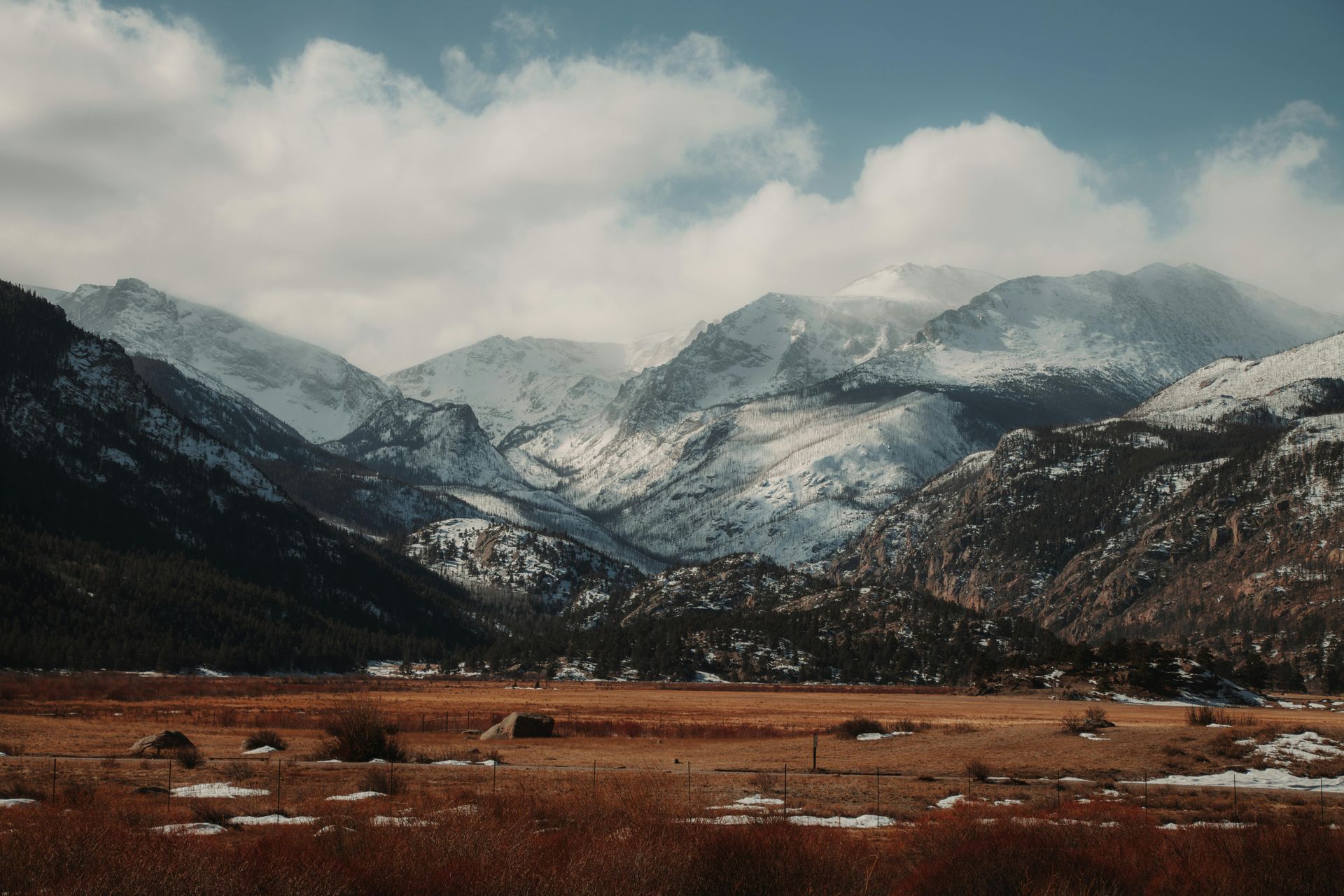 a snowy mountain landscape beyond a dead grass valley