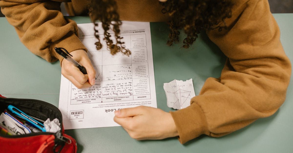 A woman is sitting at a table writing on a piece of paper with a pen.