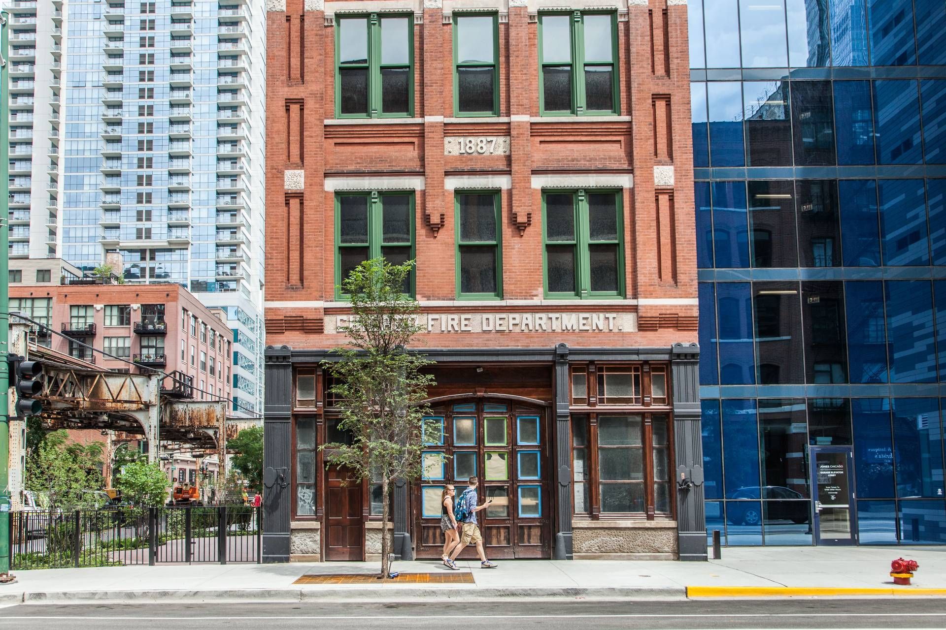 A man is walking down the sidewalk in front of a large brick building.