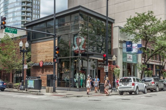 A group of people are crossing the street in front of a lululemon store.