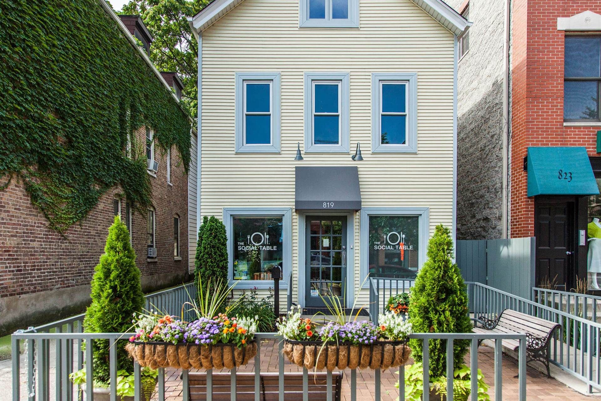A white house with a fence and flowers in front of it.