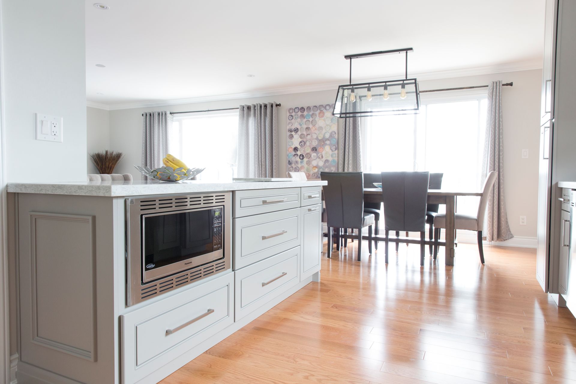 Light gray kitchen island with microwave, drawers, and a dining area in the background.