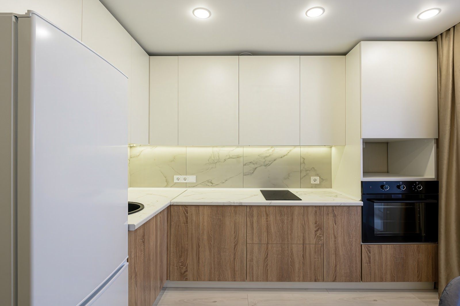 Modern kitchen with white and wood cabinets, marble backsplash, built-in oven, and a refrigerator.