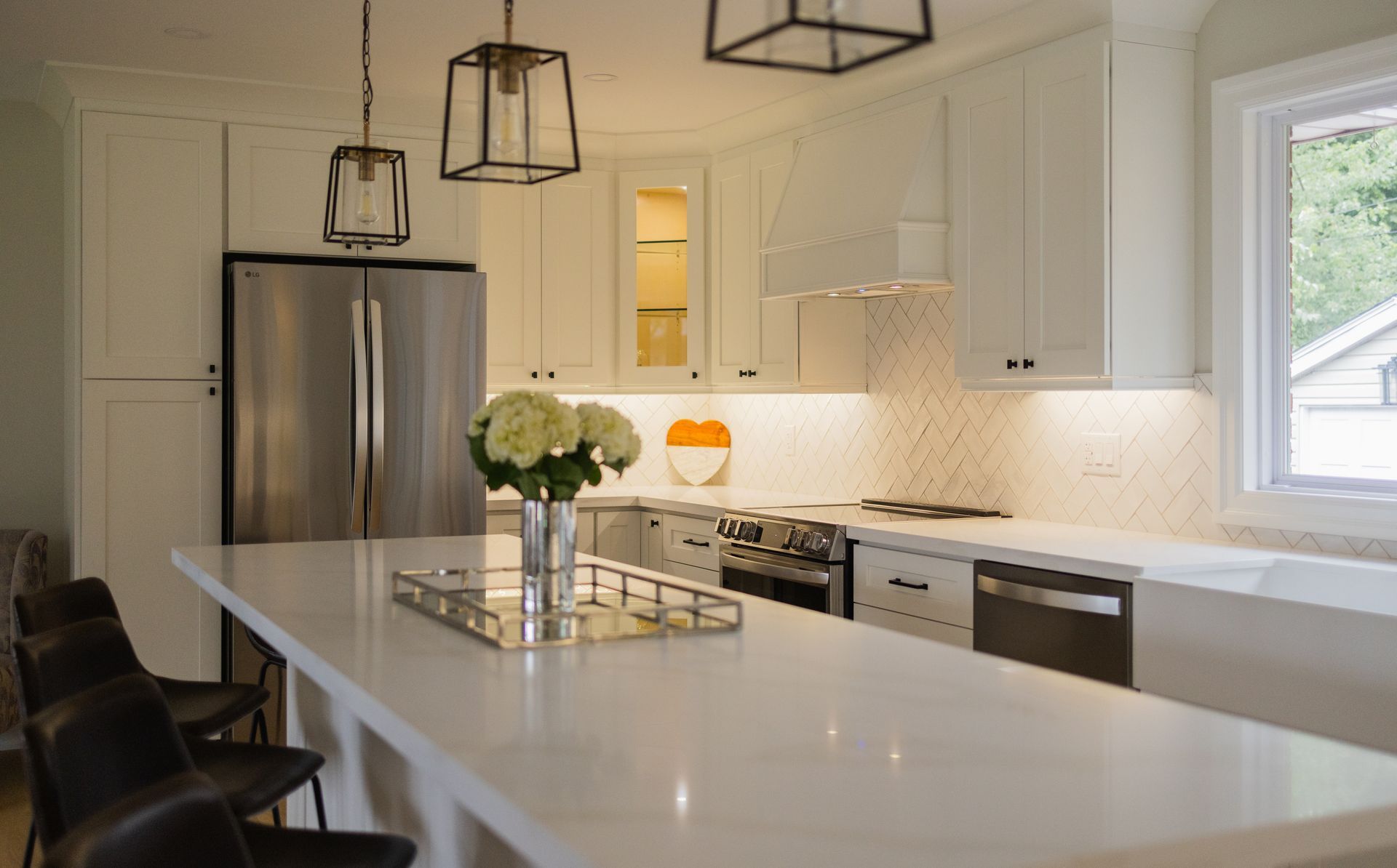 Modern white kitchen with a breakfast bar, stainless steel appliances, and pendant lighting.