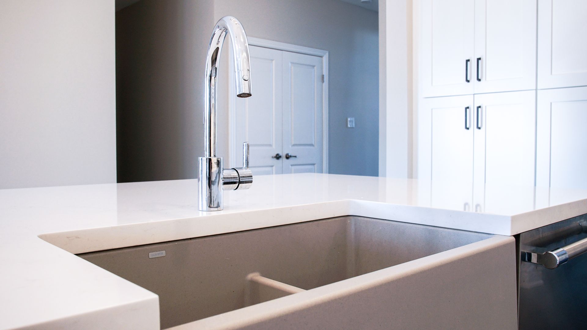 Kitchen sink with chrome faucet, white countertop, and cabinets.