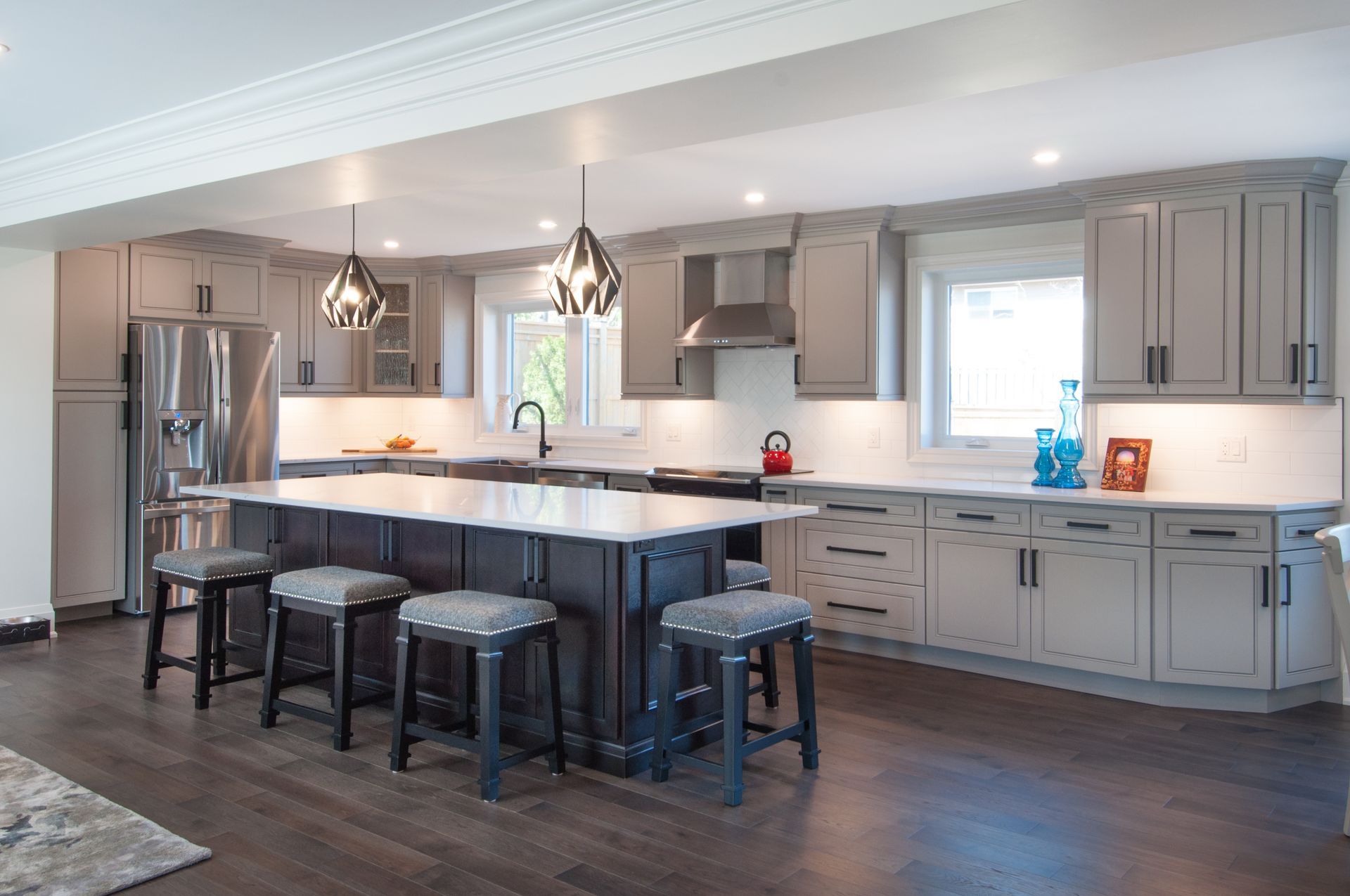 A kitchen with gray cabinets , white counter tops , stools and a large island.