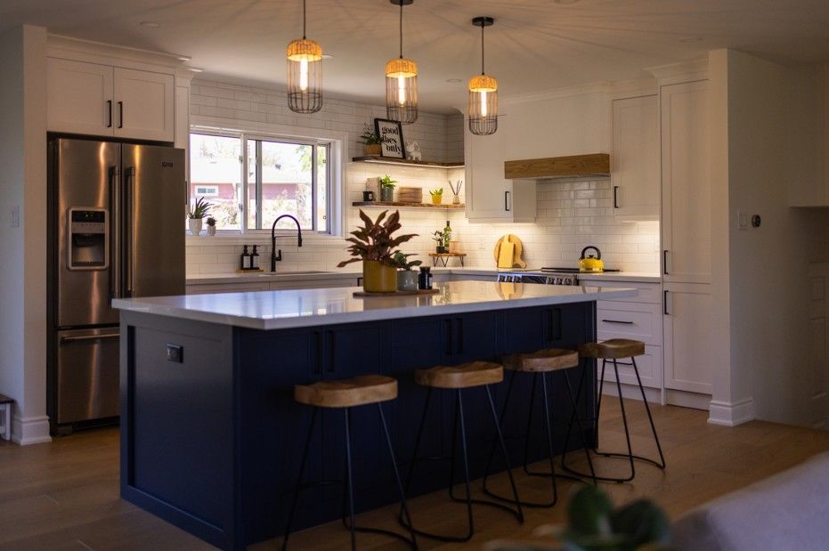Modern kitchen with navy island, white cabinets, wood accents, and pendant lights.