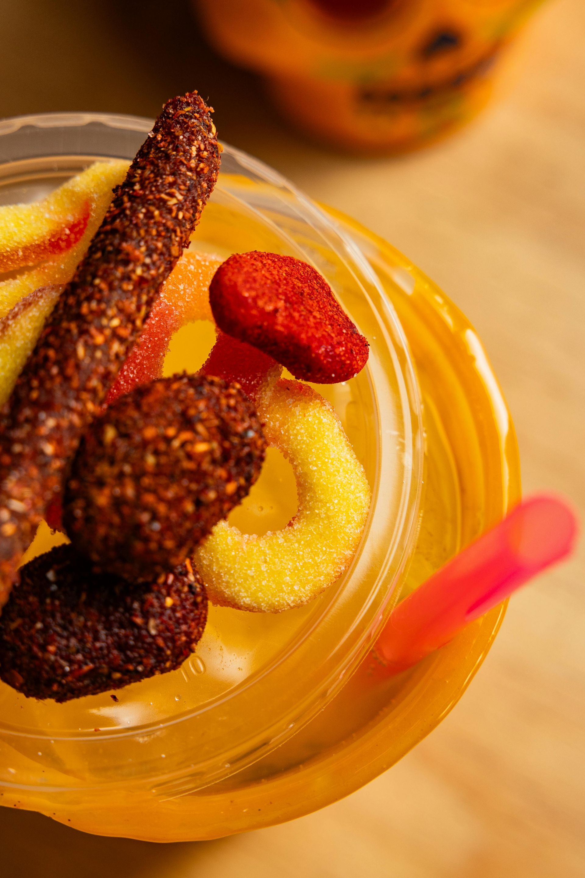 Close-up of a clear plastic cup with an orange drink, topped with sugared candies and a pink straw.