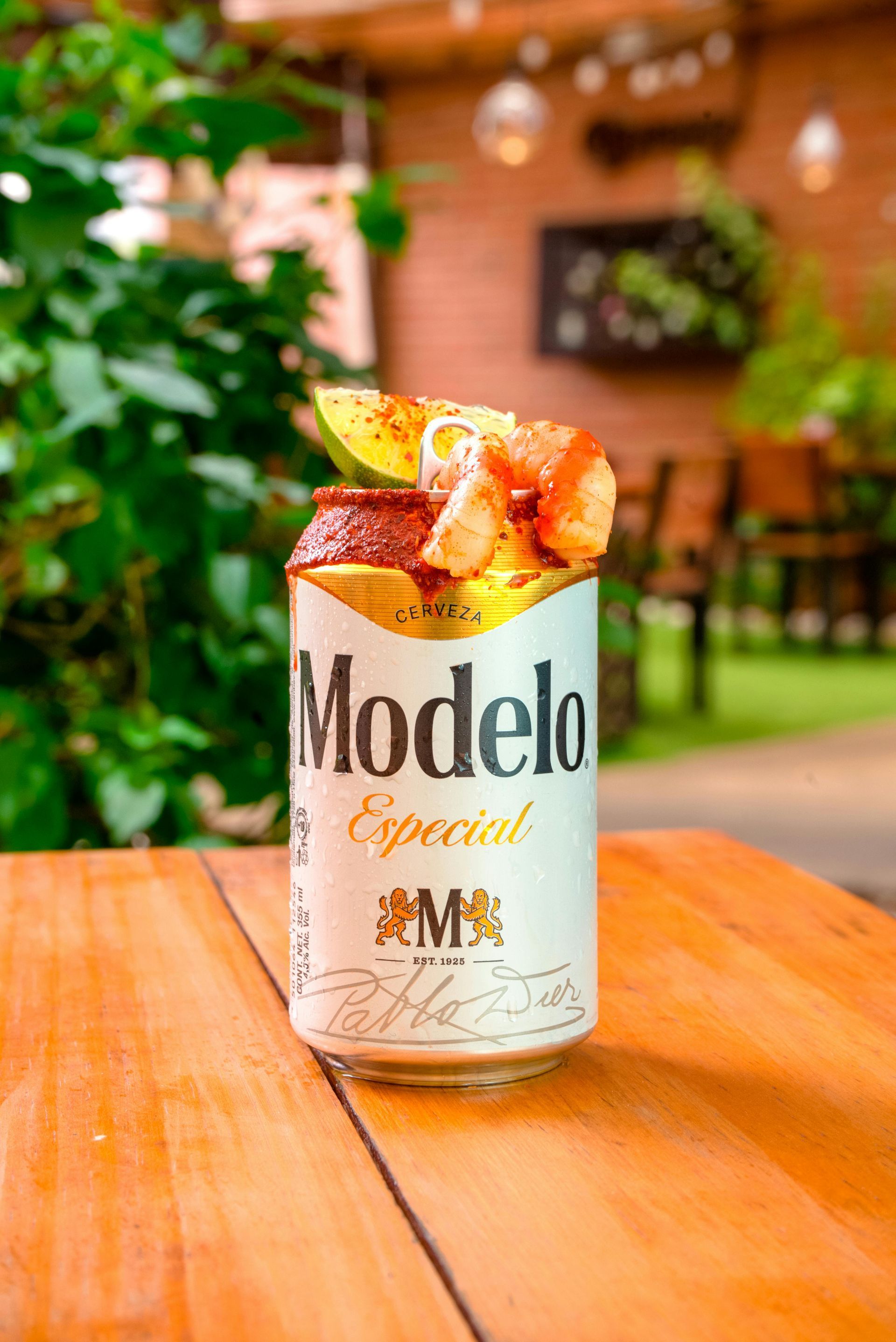 Modelo Especial beer can with toppings on a wooden table, outdoor setting.