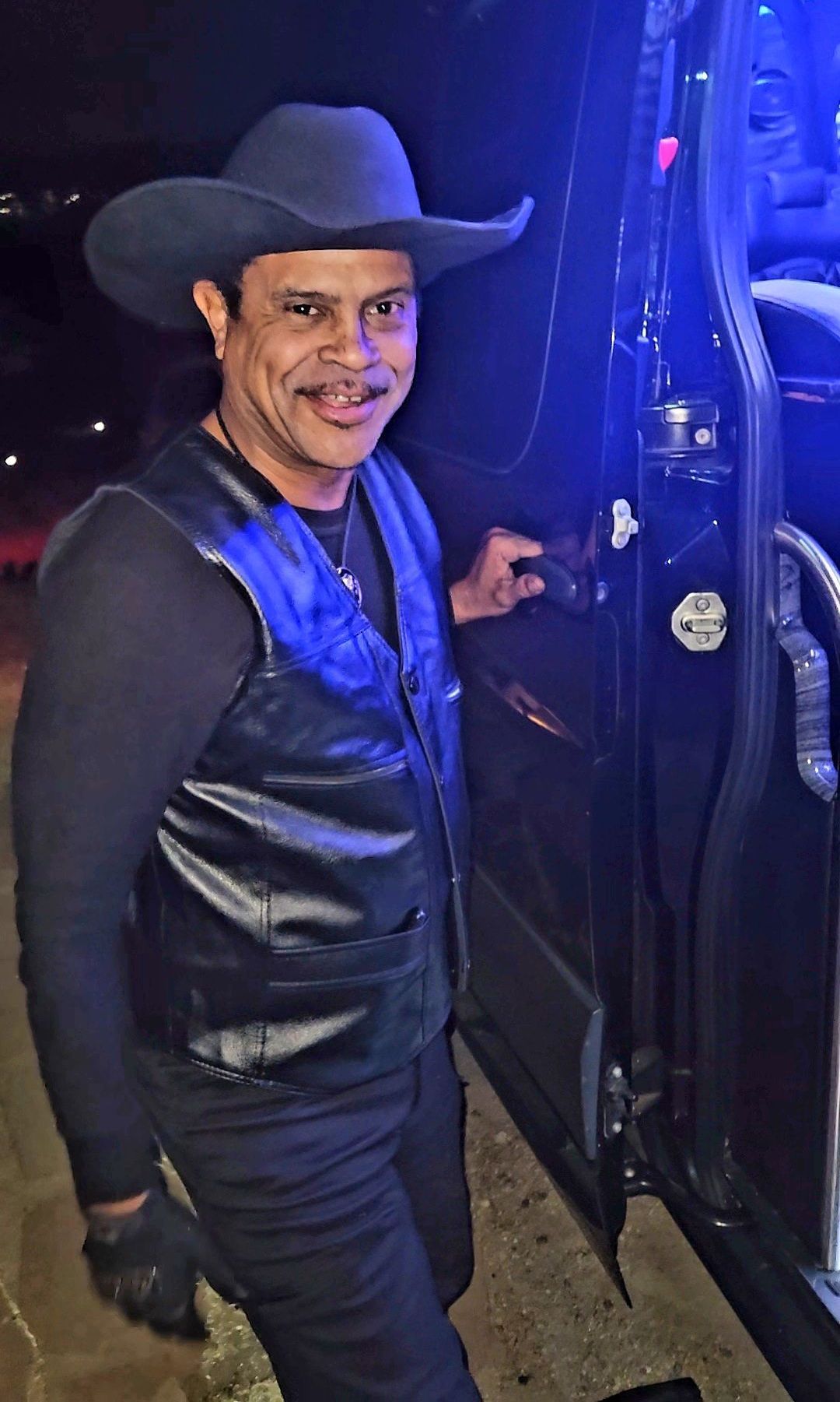 A man wearing a cowboy hat and a leather vest is standing next to a truck.