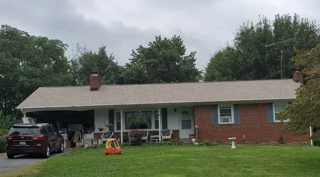 A brick house with a car parked in front of it on a cloudy day.