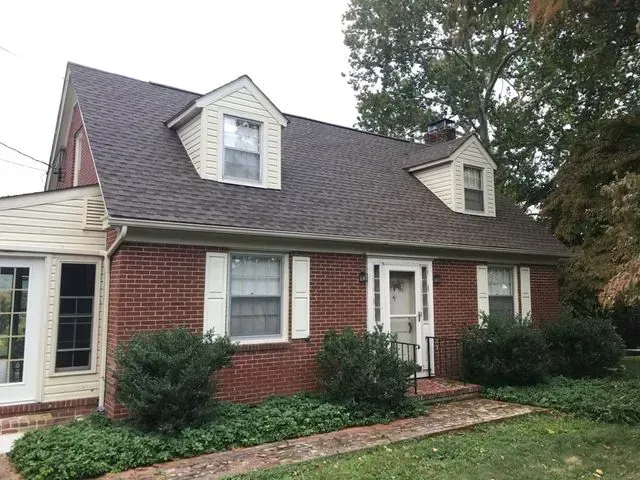 A brick house with a brown roof and white shutters