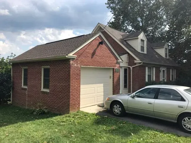 A car is parked in front of a brick house with a garage.