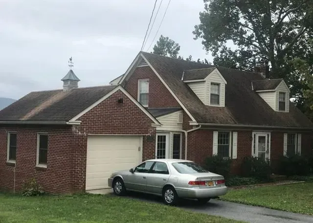 A silver car is parked in front of a large brick house.
