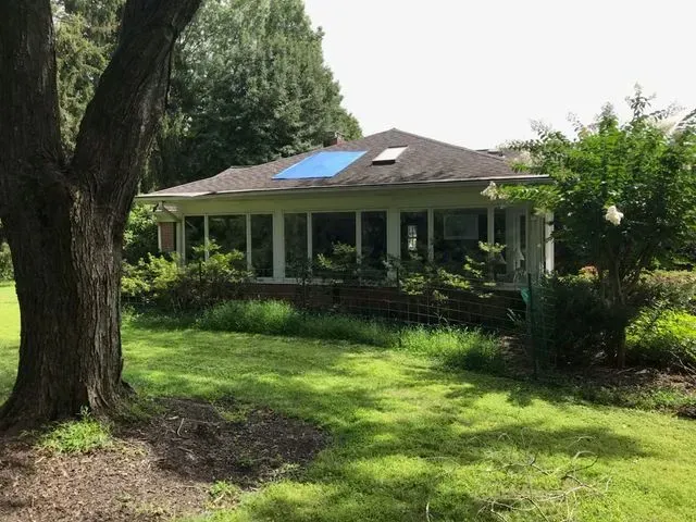 A house with a blue skylight on the roof is surrounded by trees and grass.