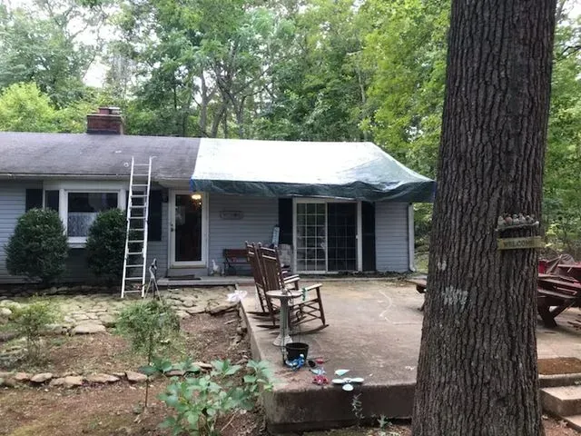 A house with a tarp on the roof is being painted.