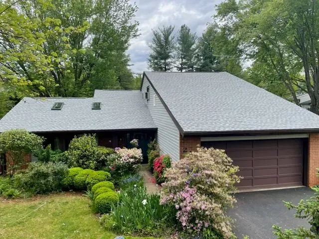 A house with a gray roof and a brown garage door is surrounded by trees.