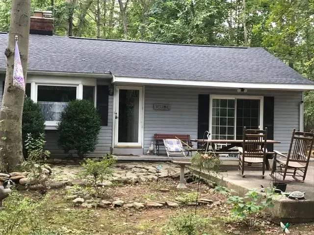 A small house with a porch and chairs in the woods.